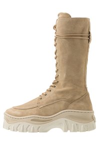 Bota larga de ante beige con frente de cordones, punta redondeada y suela de plataforma blanca gruesa que presenta acentos texturizados.