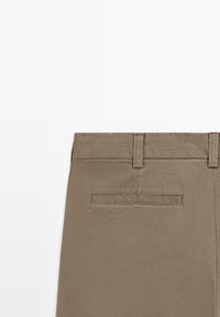 Khaki bukser har et glat stof, et slankt fit og en enkelt baglomme med klap. Taljebåndet har bæltestropper.