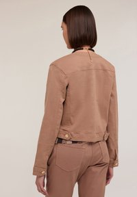 Beige denimjacka med cropped design, knapprader vid ärmarna och ryggen samt en slät yta. Bakifrån visar den en enkel, ren silhuett.