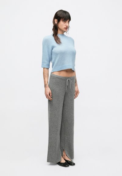 Pulover albastru deschis, scurtat, și pantaloni largi tricotati gri, cu talie ajustabilă cu șnur, prevăzuți cu deschideri laterale și textură moale.