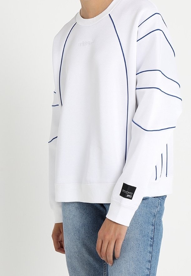 Sweatshirt blanc avec des accents et des coutures bleu marine. Présente des poignets et un ourlet côtelés, avec un patch logo sur la manche. Coupe décontractée.