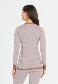 Långärmad träningströja i ljusrosa, med en texturerad tyg och maroonakcent samt kontrasterande sömmar längs sömmarna.