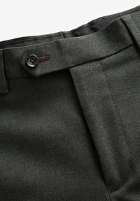 Pantalones de espiga verde oscuro con frente plano, que cuentan con un cierre de botón único y un detalle en la cinturilla a juego. Textura de tejido suave.