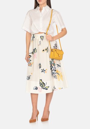 Camicia bianca corta, gonna lunga fino al ginocchio con motivo floreale in crema. Borsa a tracolla gialla. Scarpe con tacco alte marroni.
