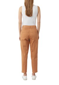 Pantaloni di cotone beige con vestibilità dritta, tasche posteriori e orli cuffi, abbinati a sneakers bianche e a una maglietta bianca senza maniche.