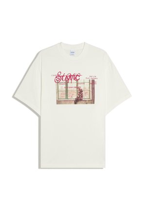 T-shirt blanc avec un graphisme représentant une personne assise sur un rebord de fenêtre et un texte rouge indiquant "STATIC" ainsi que d'autres mots plus petits au-dessus et en dessous.