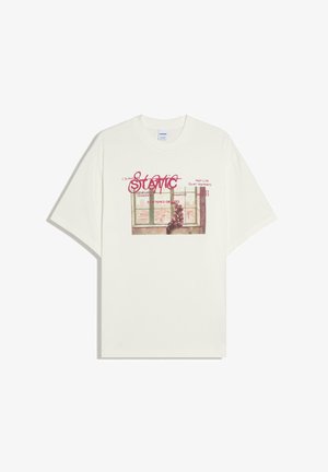 T-shirt blanc avec un graphisme représentant une personne assise sur un rebord de fenêtre et un texte rouge indiquant "STATIC" ainsi que d'autres mots plus petits au-dessus et en dessous.