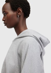 Felpa grigia con un grande cappuccio e tessuto morbido e texturizzato. La vista laterale mostra una vestibilità rilassata e dettagli di design minimalisti.
