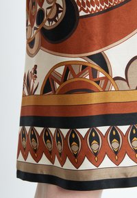 Bedruckter Rock mit kreisförmigen und geometrischen Mustern in Rost, Creme und Schwarz. Glatter Stoff mit bunten Randdetails.