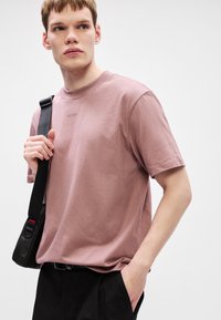 Měkké bavlněné tričko s krátkým rukávem v světlé růžové barvě, s kulatým výstřihem a jemně vyraženým logem značky vpředu.