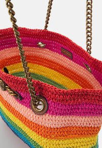 Tkaná slámová taška v duhových barvách: červené, růžové, oranžové, žluté, zelené a modré pruhy. Má bronzové řetízkové uši a očky.