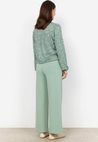 Mäta zelený top s paisley vzorom, dlhé rukávy a elastické manžety. Koordinujúce široké nohavice v jednoliatej mäta zelenej farbe a ploché topánky.