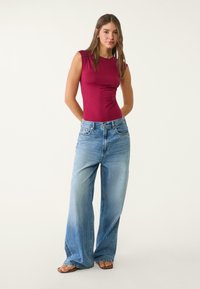 Burgunderfarbener, figurbetonter Oberteil mit kurzen Ärmeln, kombiniert mit hellblauen, weit geschnittenen Jeans. Glatte Stofftextur, lässiges Design und blaue Denim-Details.