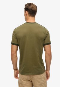 Camiseta de manga corta en verde oliva con cuello redondeado y ribete en verde oscuro en las mangas. Tela suave con un detalle mínimo.