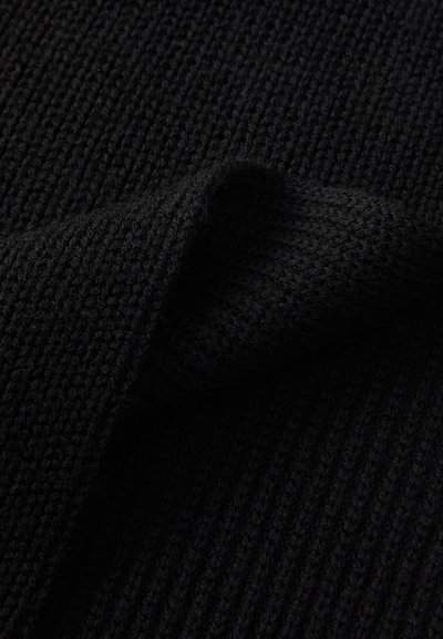 Black knitted fabric with ribbed texture and folded edge showing detailed stitch pattern and soft material.