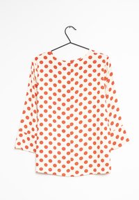 Blusa a maniche lunghe crema con grandi pois rossi, caratterizzata da un colletto rotondo e maniche leggermente svasate. Tessuto dalla texture liscia.