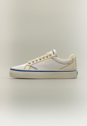 Baskets basses en toile blanche avec des accents beiges, une bande bleue sur la semelle et des œillets métalliques pour les lacets, vues de profil.