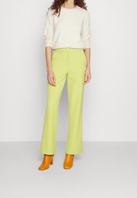 Pull crème douillet à manches longues associé à un pantalon taille haute à jambes larges d'un vert citron éclatant ; complété par des bottines à talons orange.