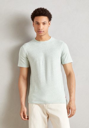T-shirt en coton vert clair avec des manches courtes, un col rond et une finition texturée. Il présente une petite étiquette logo sur le bas de l'ourlet.