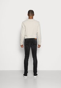 Sweatshirt cinza claro com gola redonda, combinada com jeans pretos de corte justo e ténis brancos. Design simples com um acabamento texturizado.