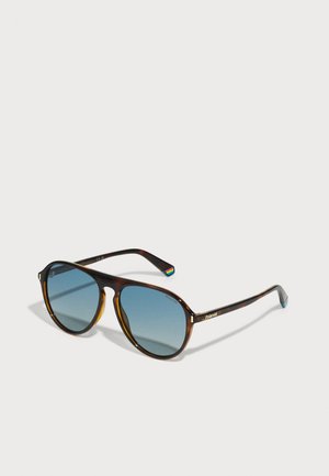 Óculos de sol tartaruga com lentes de gradiente azul, forma arredondada, detalhe do logotipo dourado na armação e um acento colorido na extremidade da haste.