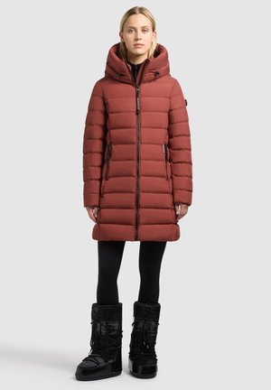 Red puffer coat with a high collar and hood, featuring a front zipper, two side pockets, and ribbed texture. Worn with black snow boots.