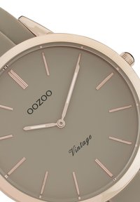 Montre ronde grise avec un bracelet en silicone lisse. Marqueurs d'heure et aiguilles en or rose. Texte noir "OOZOO" et "Vintage" sur le cadran.
