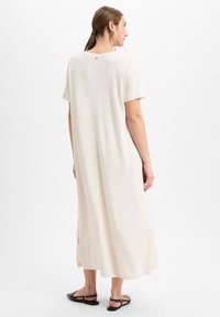 Langes, cremefarbenes Kleid aus einem weichen Stoff. Hat kurze Ärmel, einen runden Ausschnitt und ein kleines Knopfdetail auf der Rückseite.