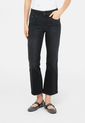 Jeans di denim neri con una vestibilità dritta, caratterizzati da dettagli testurizzati con borchie metalliche sulle tasche anteriori. Abbinati a ballerine nere.