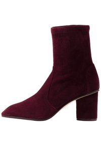 Botín de ante burdeos con caña ajustada, punta puntiaguda y tacón grueso. Presenta un diseño sin costuras con costuras mínimas.