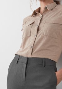 Beżowa, krótko rękawowa koszula zapinana na guziki z dwoma kieszeniami na piersiach oraz szare dopasowane spodnie z kieszeniami, o slim fit i gładkiej fakturze.