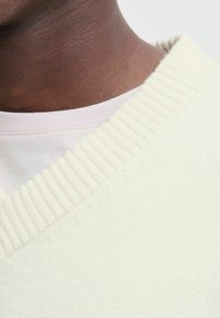 Close-up of a person’s neck and upper chest wearing a white ribbed sweater over a light pink crew neck shirt.