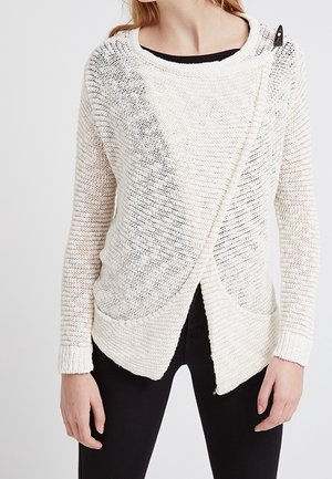 Pull en tricot blanc avec un design croisé lâche, présentant un motif texturé, un large col et deux poches avant.