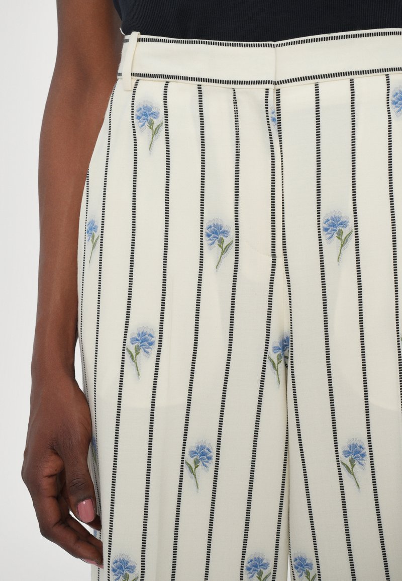 Cream trousers with vertical black stripes and light blue floral embroidery, featuring a smooth texture and a fitted waistband.