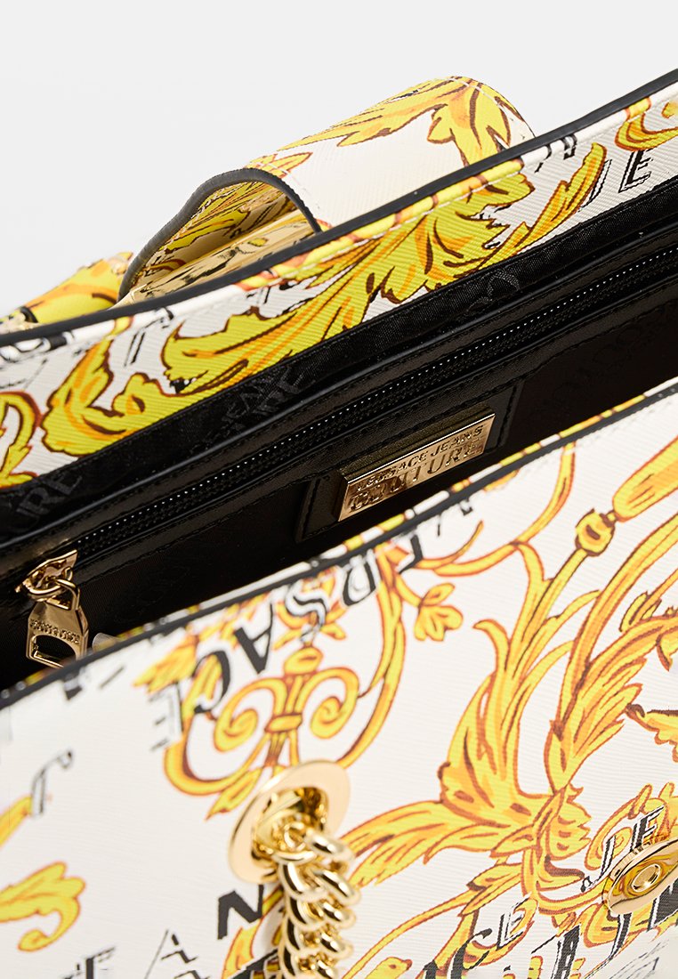 Weiße Handtasche mit auffälligen gelben und schwarzen Blumenmustern. Goldfarbener Kettenakzent und Reißverschluss. Strukturierten Oberfläche. Innenfutter in Schwarz.