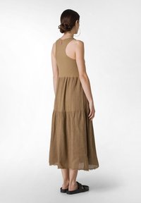 Hnědá maxi šaty s tiered stylem, ribbed živůtkem a surovým lemem. Mají design s racerback a jsou doplněny černými sandály.