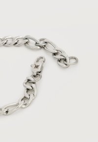 Ασημένιο μεταλλικό βραχιόλι με μεγάλα οβάλ συνδετικά και κούμπωμα με εγχάρακτο λογότυπο σε απλό ανοιχτό φόντο.