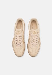 Beiga Adidas-sneakers med en slät läderöverdel, rund tå, tonala snören, tre sidostrecken och en texturerad gummisula.