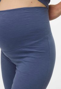 Leggings de maternité bleu marine fabriqués en matériau doux et extensible. Ils présentent une taille haute et une texture lisse et uniforme avec un léger brillant.