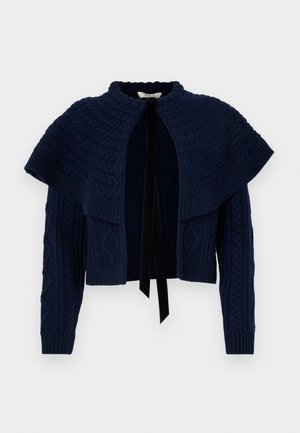 Mørkeblå strikket cardigan med et tekstureret kappe-design, der har høj krave og sort bånd-lukning. Kabelmønstre på ærmerne.