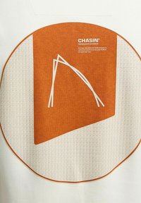 Fehér szövet, amelyen egy nagy, kör alakú narancssárga grafika található, geometrikus mintázattal és fehér vonalakkal. A szöveg így szól: "CHASIN' PERFORMANCE JEANSWEAR."