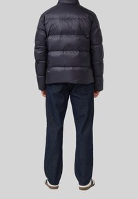 Mornarska jakna s punjenjem, s horizontalno prošivenim sekcijama, visokim ovratnikom i glatkom završnom obradom, u kombinaciji s tamnim trapericama i bijelim tenisicama.