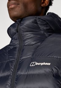 Jachetă puffer bleumarin din material lucios, cu guler înalt, închidere cu fermoar și logo-ul alb Berghaus pe piept.
