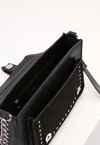 Clutch bag in pelle nera con borchie metalliche, tracolla a catena e compartimenti aperti che mostrano una tasca con zip all'interno, su uno sfondo bianco.