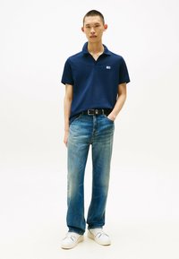 Polo navy de manga corta, corte relajado, combinado con jeans de mezclilla azul claro y zapatillas blancas. El cinturón tiene un detalle de hebilla de metal.