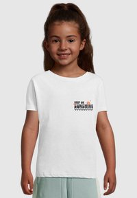 Witte T-shirt met korte mouwen, voorzien van de tekst "KEEP ON SUNSHINE" met bloem- en geruiten accenten aan de voorkant. Katoenen stof, casual ontwerp.