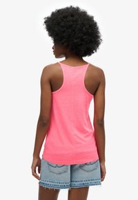 Roze mouwloos topje met een racerback-ontwerp, gemaakt van lichtgewicht materiaal. Gecombineerd met lichtblauwe denim shorts met rafelige randen.