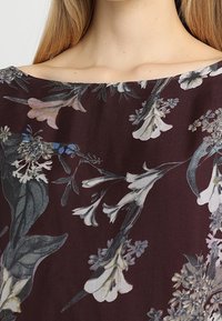 Odzież w kwiatowy wzór z głębokim burgundowym tłem, zdobiona białymi i niebieskimi kwiatami. Gładka tkanina z luźnym dekoltem.