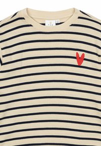Top crema con righe blu, scollatura rotonda e un cuore rosso ricamato sul lato sinistro. Tessuto morbido, design casual.