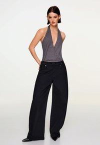 Top gri cu barete ajustabile și textură în dungi, asortat cu blugi negri cu talie înaltă și picioare largi. Modelul stă cu mâinile în buzunare, purtând pantofi cu toc ascuțit.